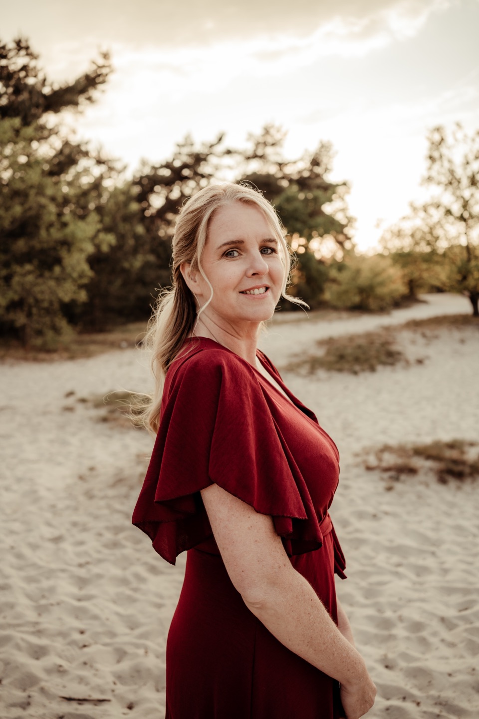 Portretfoto van Cindy, glimlachend in een rode jurk buiten in de natuur